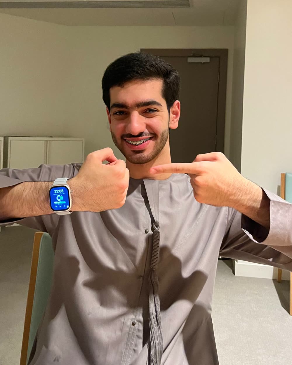 Ali, a student who is hard of hearing, smiling and pointing at WristEcho on his wrist